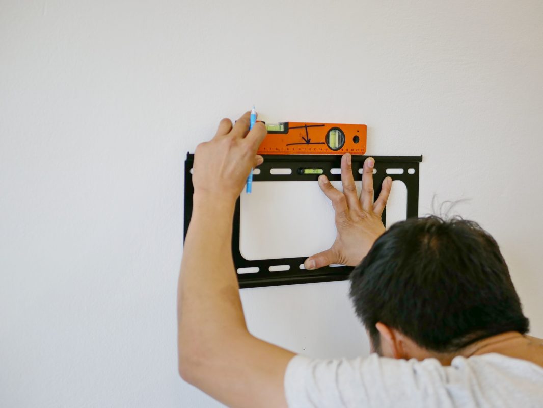 Technician preparing to mount a TV on a plaster wall by marking stud positions.