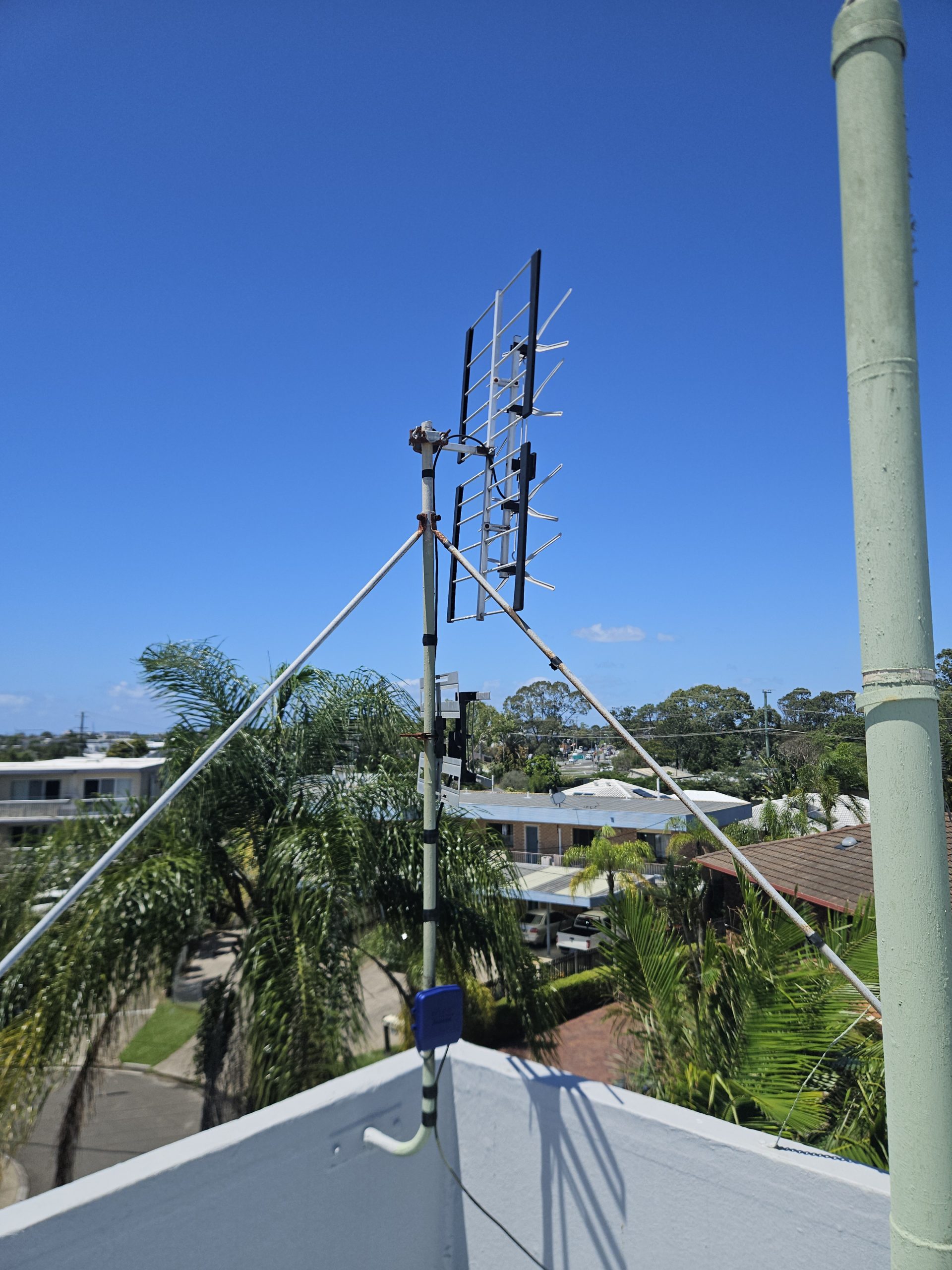 Rooftop TV antenna system installed on a home in Sunshine Coast with surrounding trees and cloudy sky.