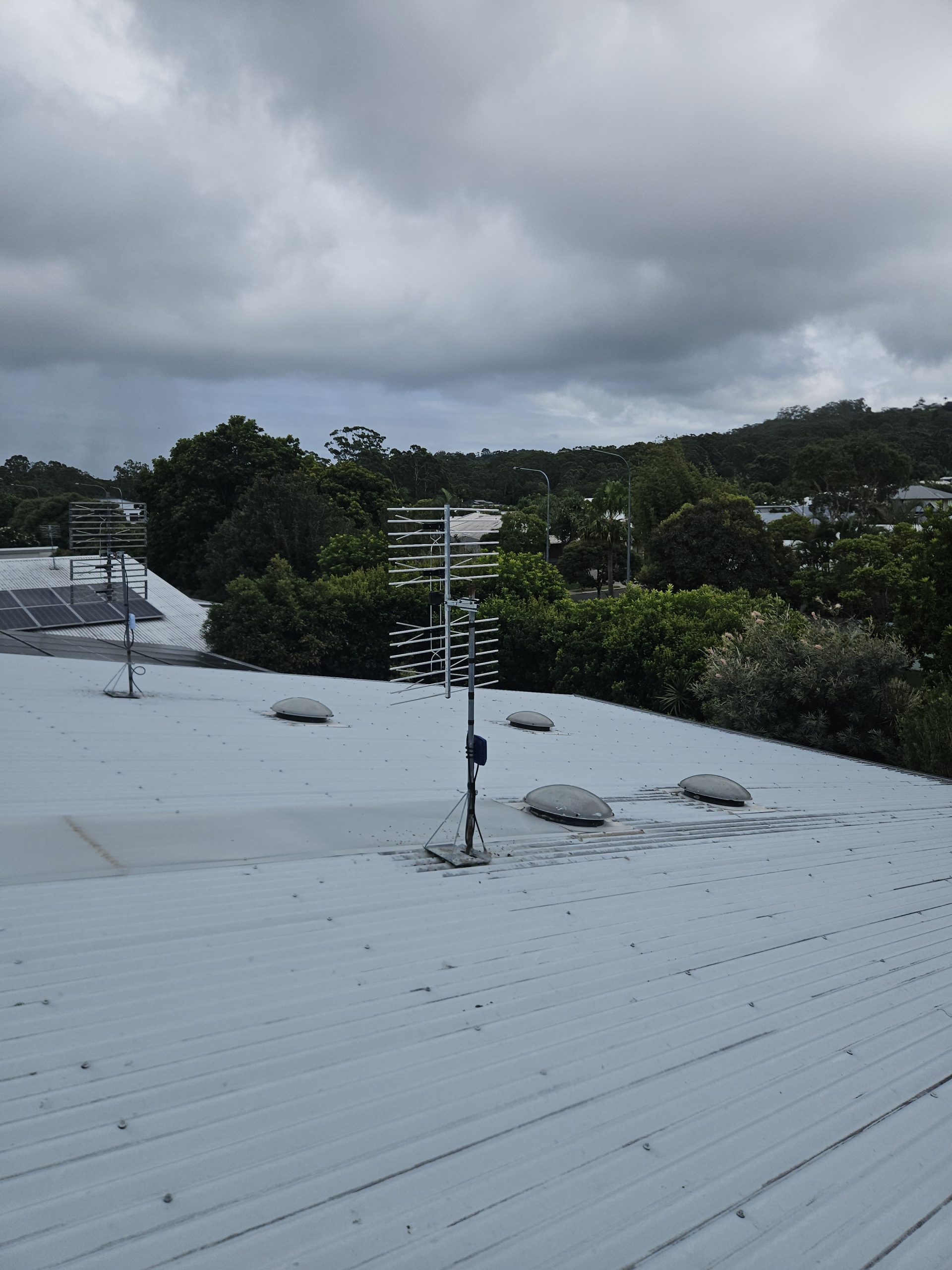 Rooftop TV antenna installation on Sunshine Coast with cloudy sky and residential area.